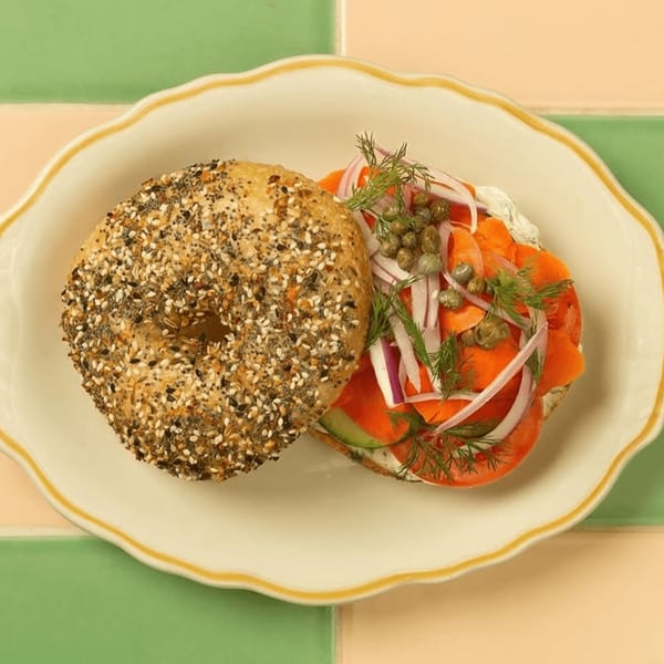 Everything bagel with cream cheese, smoked salmon, red onion, capers, and dill on a white plate.