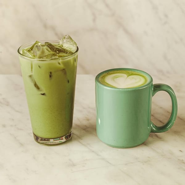 An iced matcha latte and a hot matcha latte with heart-shaped foam on a marble surface.