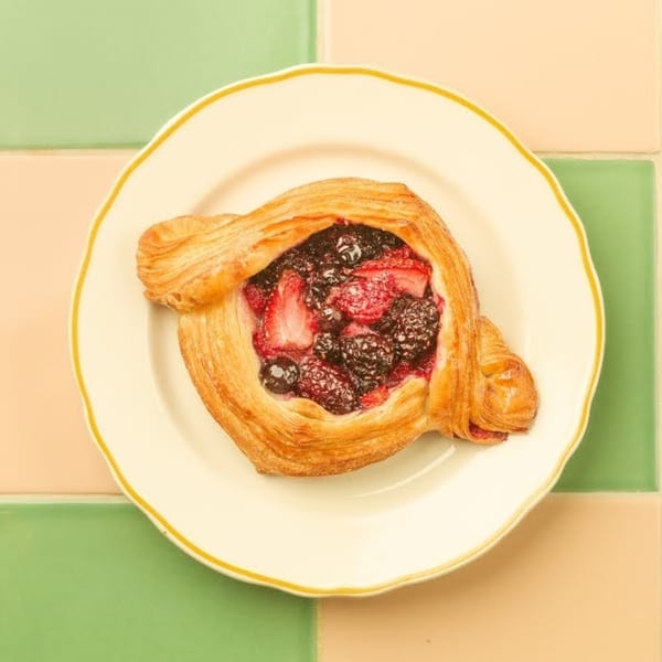 A golden-brown Kitchen Mouse fruit danish with mixed berries on a white plate.
