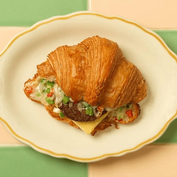 A croissant breakfast sandwich with sausage, melted cheese, and diced peppers on a scalloped plate.