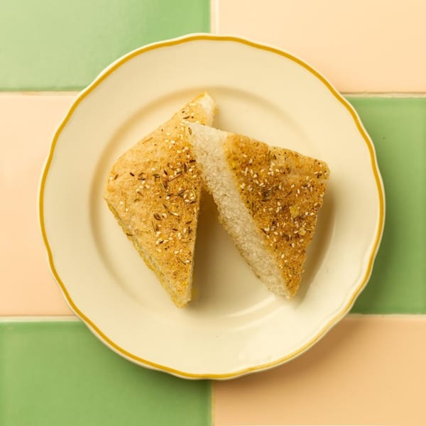 Two triangular pieces of cornbread, topped with seeds, on a white plate with a gold rim.