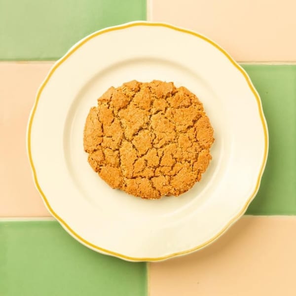 A single Kitchen Mouse breakfast cookie with a crinkled top on a white plate with a yellow rim.