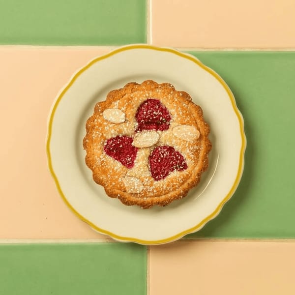A raspberry almond tart with powdered sugar on a white plate with a yellow rim.