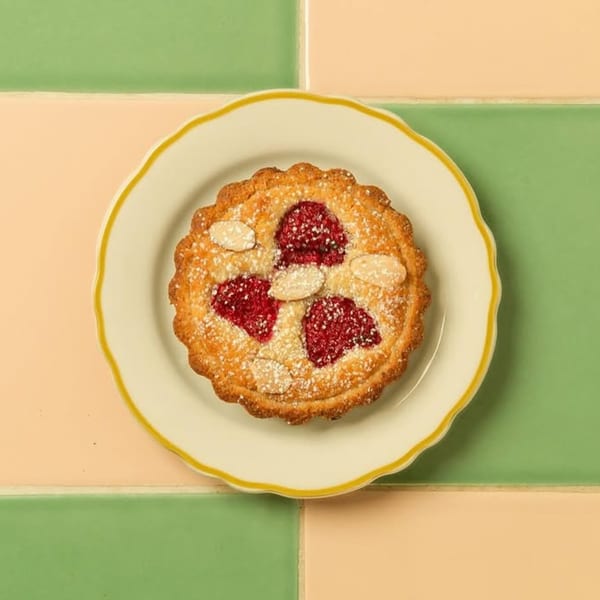 A raspberry and almond tart with powdered sugar on a white plate with a yellow rim.